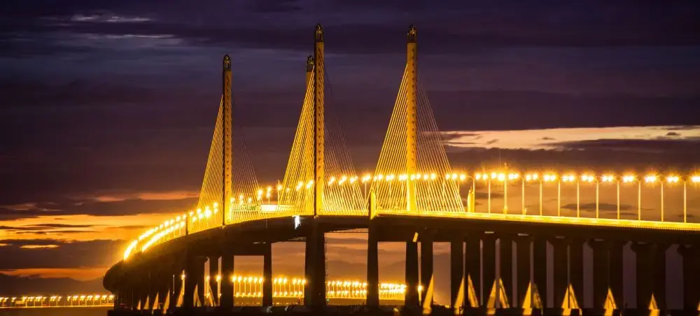Illuminated Penang Bridge spanning across water at sunset, showcasing Malaysia's modern infrastructure