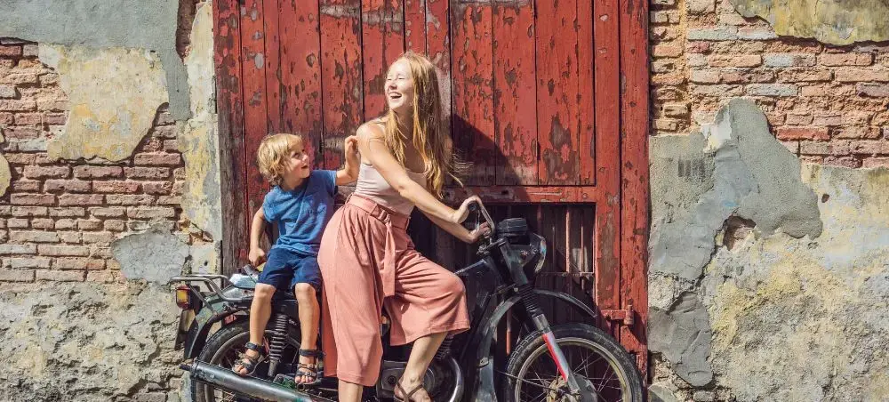 Mother and child enjoying vintage motorcycle adventure in historic Penang streets with weathered walls