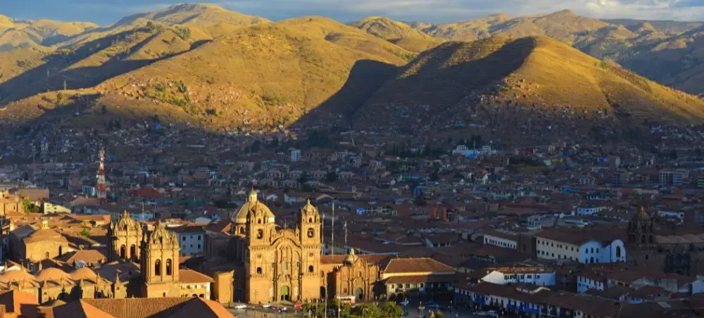 Golden sunset illuminates Cusco's colonial cathedral and red-tiled rooftops against dramatic Andean peaks