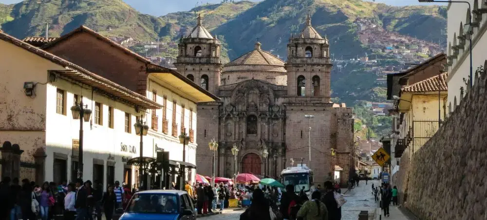 Historic colonial church with twin bell towers dominates bustling Cusco street scene with Andes mountains backdrop
