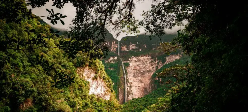 Dramatic waterfall cascading through lush green canyon in Peru, framed by tropical vegetation and misty cliffs