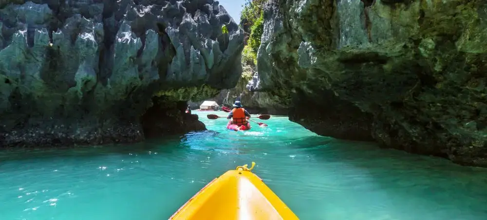 Kayakers exploring emerald lagoon through limestone caves in Philippines tropical paradise destination