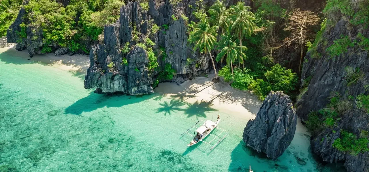 Secluded tropical beach cove in Philippines with turquoise waters, limestone cliffs, and traditional boat