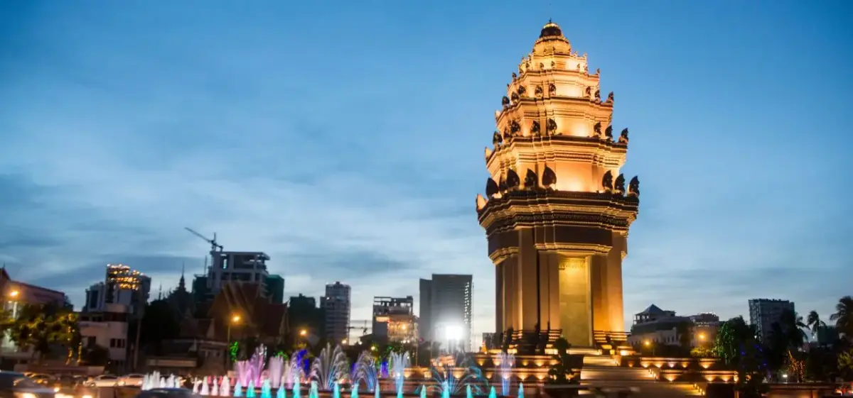 Independence Monument illuminated at dusk with colorful fountains and Phnom Penh skyline in Cambodia