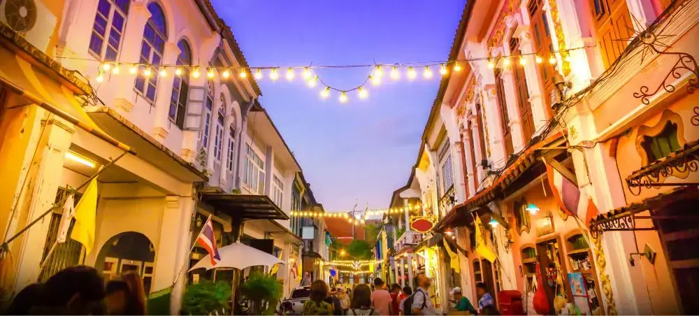 Colorful colonial shophouses line bustling Phuket Old Town street at twilight with string lights overhead