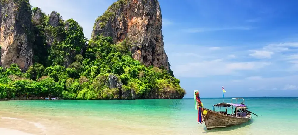 Traditional longtail boat anchored in turquoise waters near dramatic limestone cliffs in Phuket Thailand