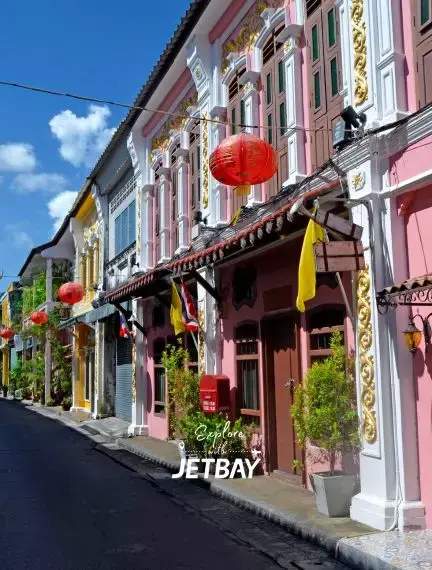 Colorful Sino-Portuguese shophouses with red lanterns line historic Phuket Old Town street under blue sky