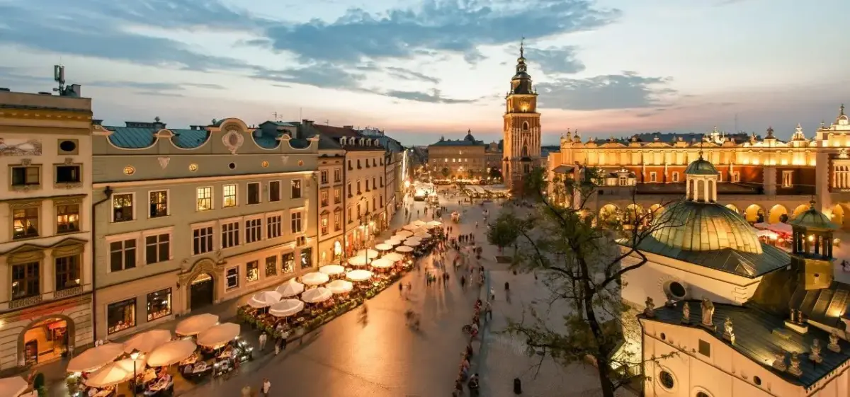 Krakow's historic Main Market Square at golden hour with illuminated medieval architecture and bustling cafes