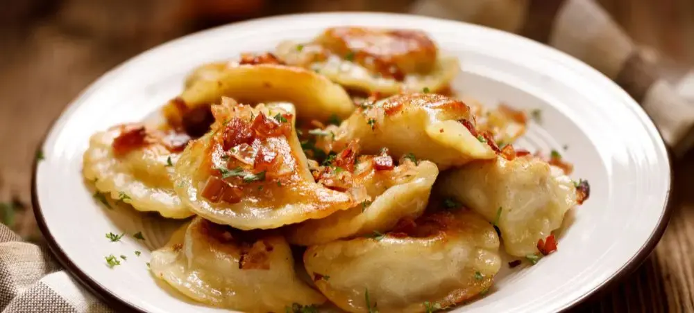 Traditional Polish pierogi dumplings with caramelized onions and herbs served on elegant white plate