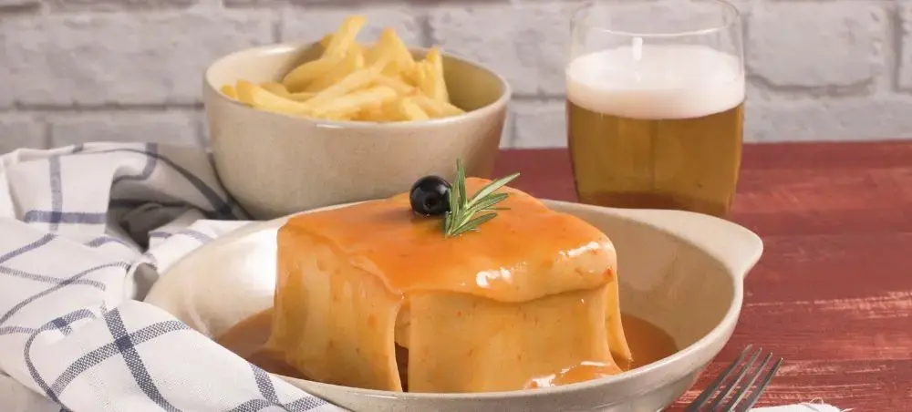 Francesinha sandwich with melted cheese and sauce served with crispy fries and beer in Porto restaurant