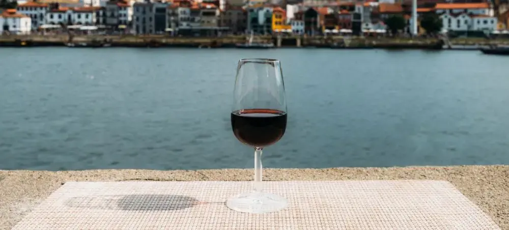 Glass of red wine overlooking Porto's historic waterfront and colorful riverside buildings in Portugal