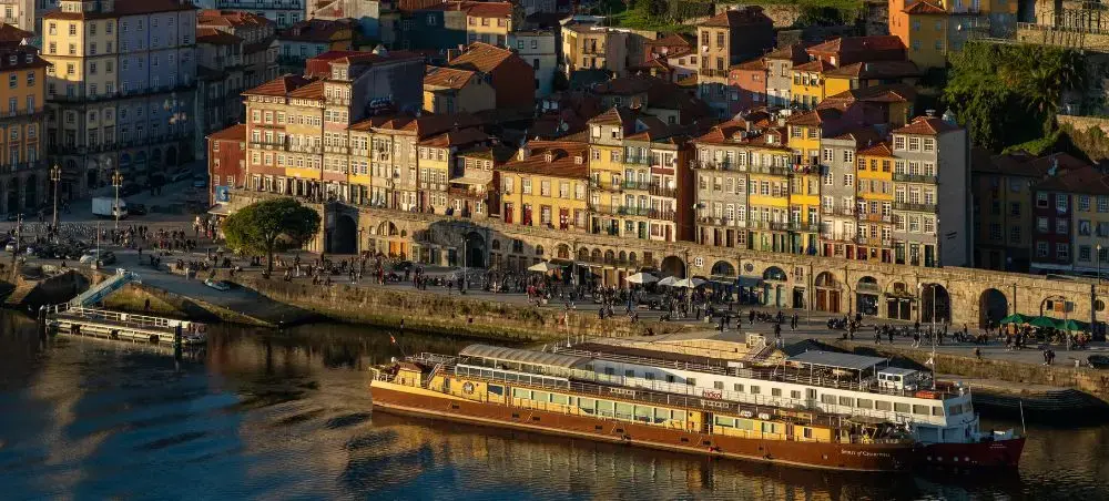 Golden hour view of Porto's historic Ribeira district with colorful buildings and Douro River cruise boat