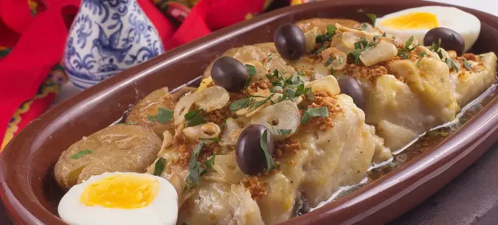Traditional Portuguese bacalhau cod dish with olives, eggs, and herbs in ceramic serving dish