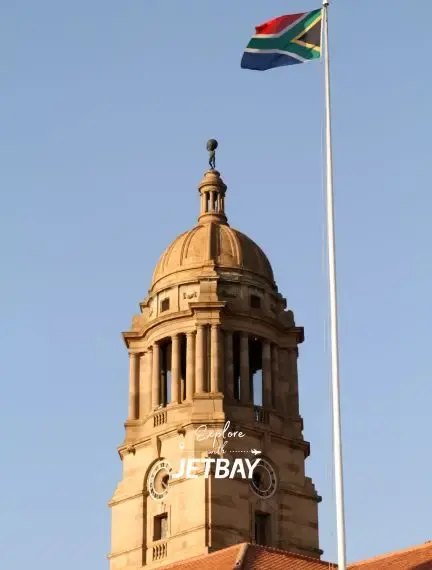 Historic sandstone clock tower with South African flag flying above in Pretoria's city center