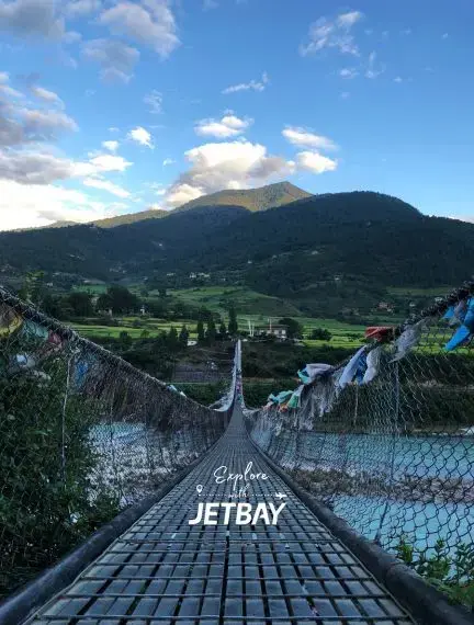 Suspension bridge crossing turquoise river in Punakha valley with traditional prayer flags and mountains