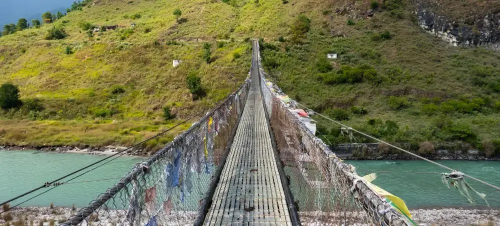 Traditional suspension bridge crossing turquoise river in Punakha valley with lush green hills