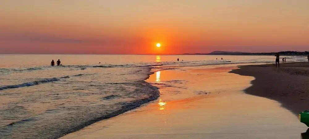 Golden sunset over Punta del Este beach with gentle waves and silhouettes of people enjoying the shoreline