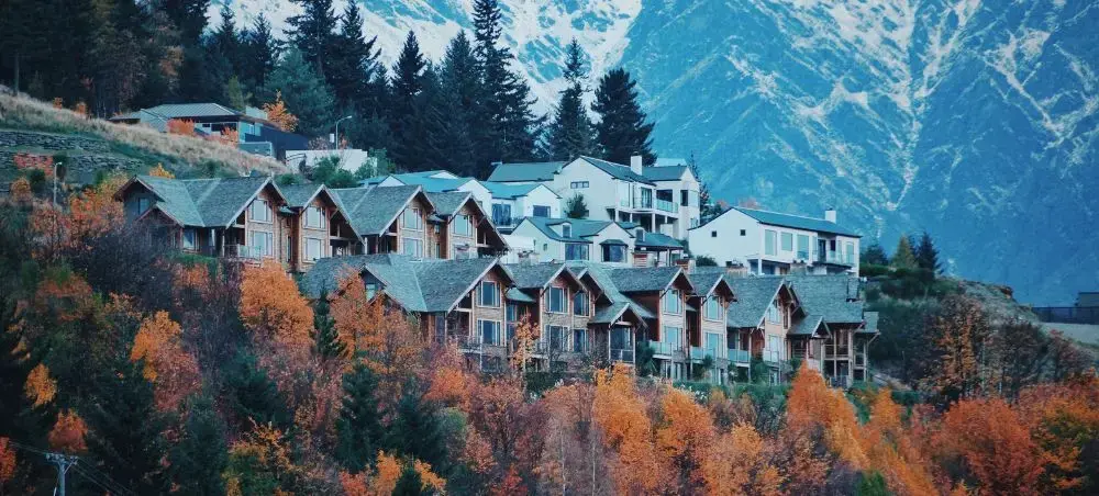 Luxury alpine chalets nestled among autumn foliage with snow-capped mountains overlooking Queenstown