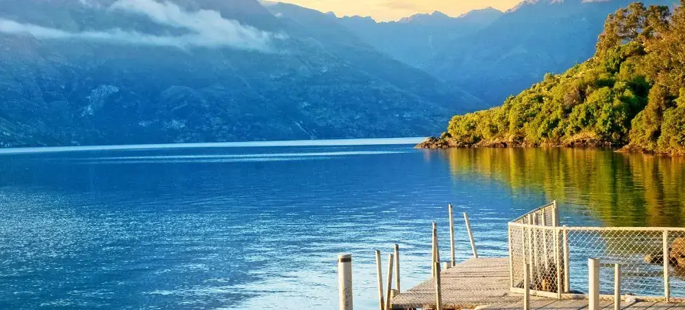 Pristine lake surrounded by dramatic mountains and lush forests near Queenstown, New Zealand's adventure capital