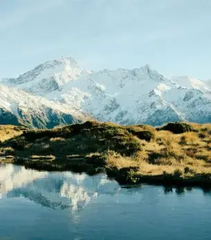 Snow-capped Southern Alps mountains reflecting in pristine lake waters near Queenstown, New Zealand