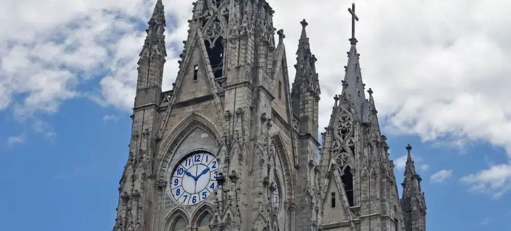 Gothic spires and clock tower of Basilica del Voto Nacional cathedral in Quito Ecuador under cloudy sky