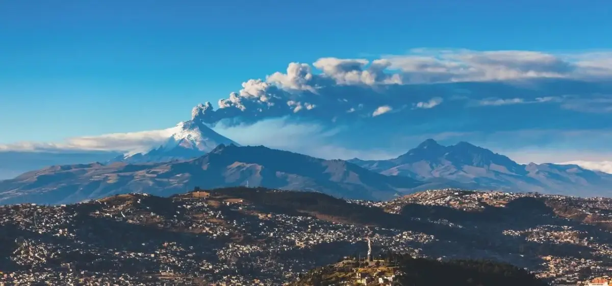 Dramatic volcanic landscape with active Cotopaxi volcano erupting above Quito's hillside neighborhoods in Ecuador