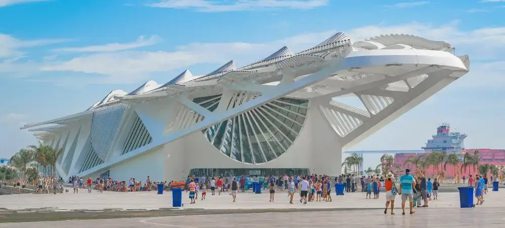 Modern architectural landmark with dramatic white curved structure and visitors exploring the waterfront plaza in Rio de Janeiro