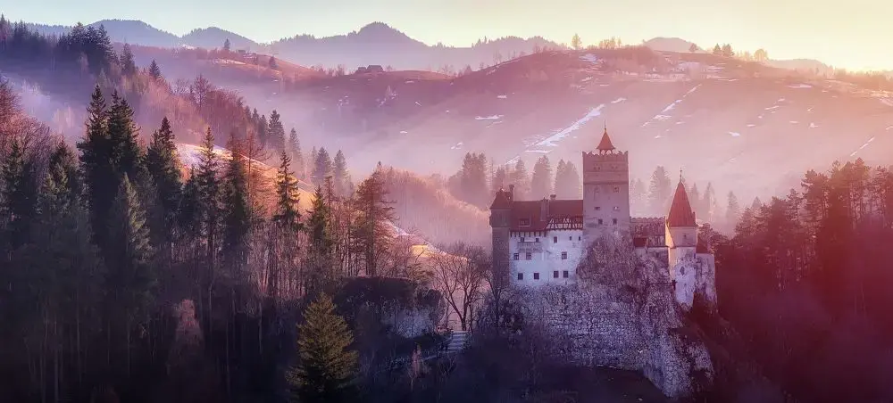 Bran Castle nestled in misty Carpathian Mountains at sunrise, showcasing Romania's dramatic landscapes