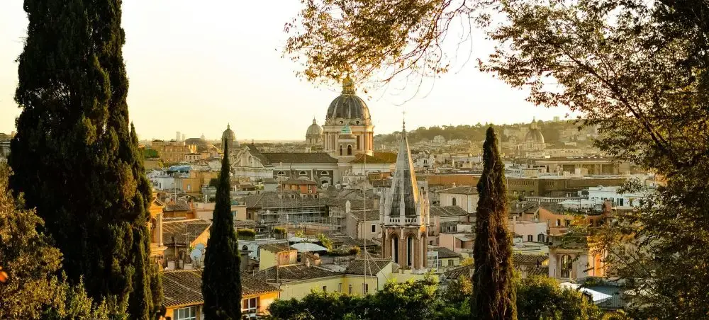 Golden hour panoramic view of Rome's historic skyline with ancient domes and cypress trees framing the cityscape