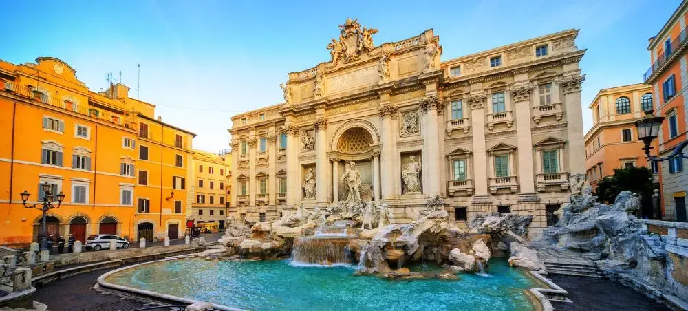 Trevi Fountain's baroque architecture and turquoise waters surrounded by golden Roman buildings at sunset
