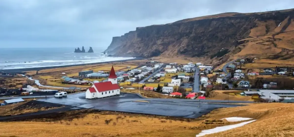 Aerial view of Saint Pierre coastal village with red-roofed church, dramatic cliffs, and black sand beach
