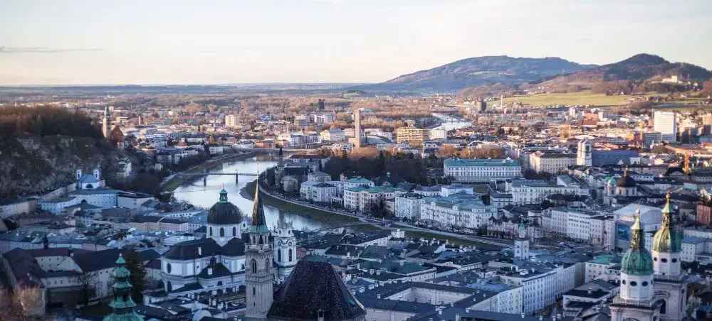 Panoramic view of Salzburg's historic old town with baroque churches, Salzach River, and Alpine foothills
