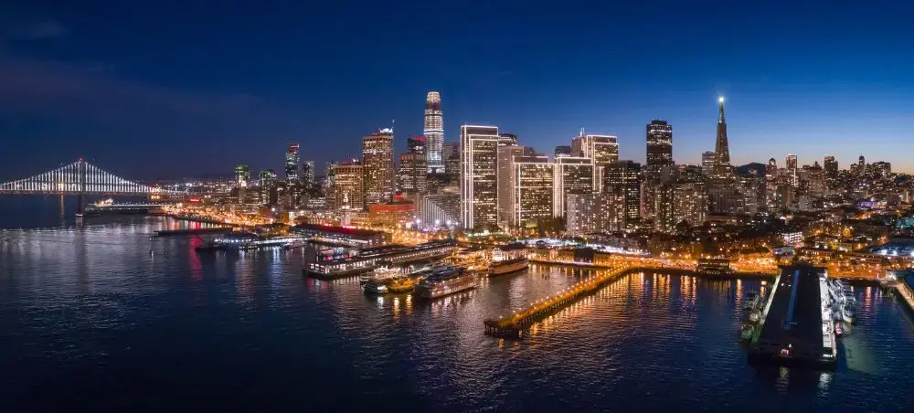 San Francisco skyline illuminated at twilight with Bay Bridge and waterfront piers reflecting in calm waters