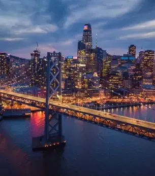 San Francisco skyline at twilight with Bay Bridge illuminated over water for luxury jet charter