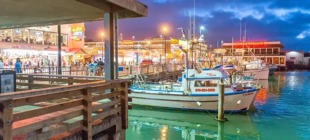 Bustling San Francisco waterfront marina with fishing boats and illuminated pier restaurants at twilight