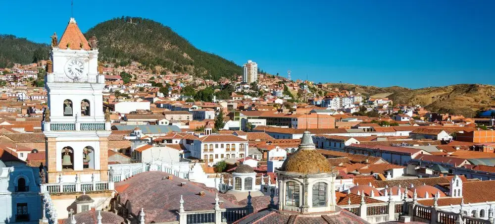Historic colonial architecture and bell tower overlooking Sucre's red-tiled rooftops with Andes mountains