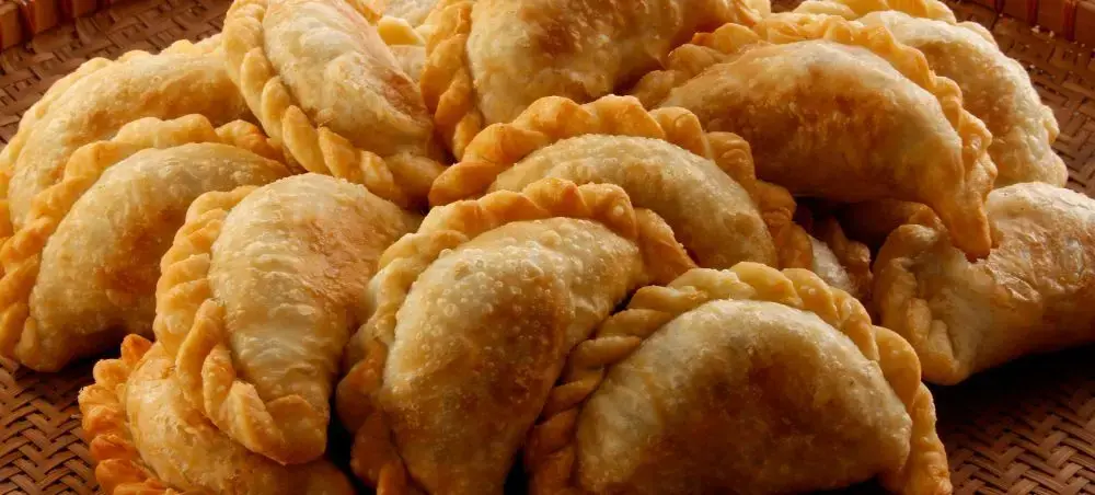 Golden empanadas with crimped edges arranged on woven basket, showcasing traditional Chilean cuisine in Santiago