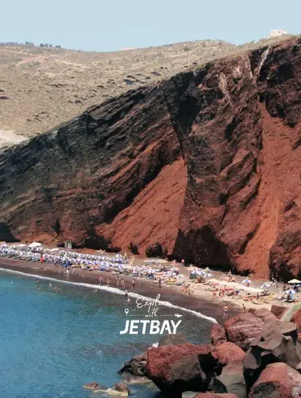 Dramatic red cliffs and volcanic beach at Santorini's famous Red Beach with sunbathers and crystal blue waters