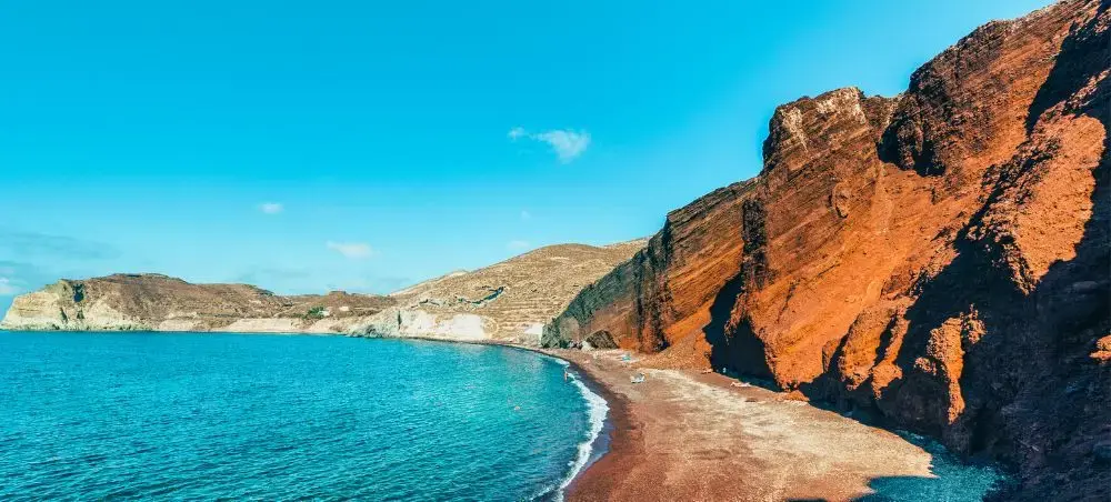 Dramatic red volcanic cliffs frame a pristine beach with turquoise waters in Santorini, Greece