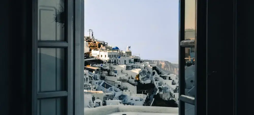 Panoramic view of Santorini's iconic white-washed buildings cascading down cliffsides through open window