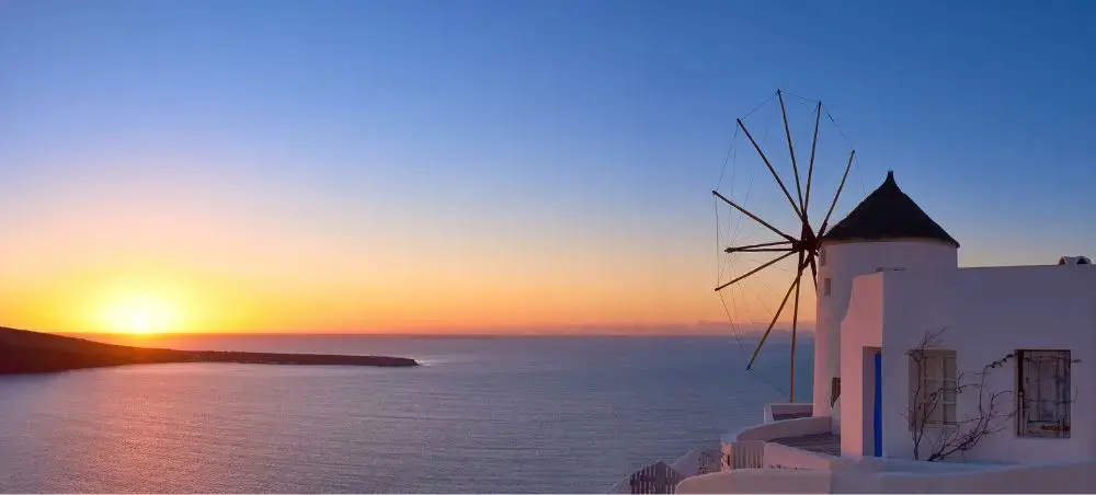 Traditional white windmill overlooking Santorini's caldera at golden sunset, showcasing Greece's iconic Cycladic architecture