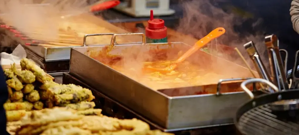 Traditional Korean street food cooking on hot griddle with golden corn dogs and steaming sauces in Seoul