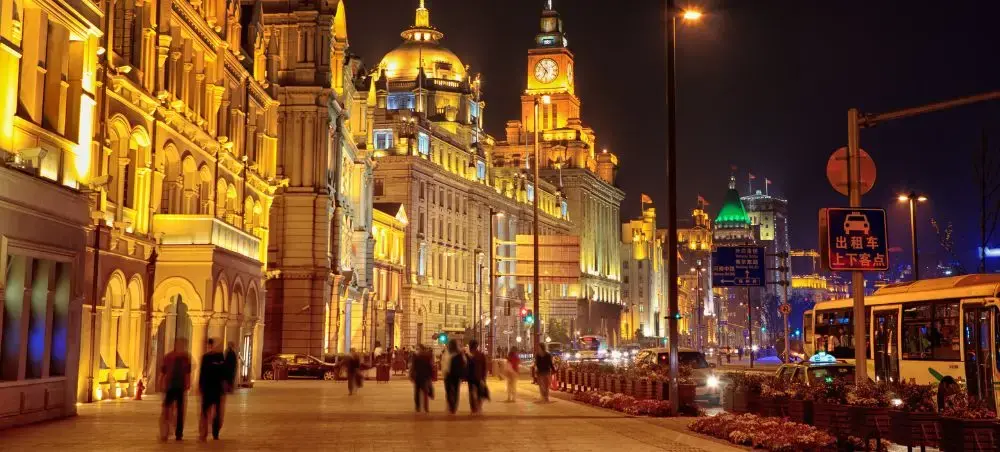 Shanghai's historic Bund waterfront illuminated at night with colonial architecture and bustling pedestrian activity