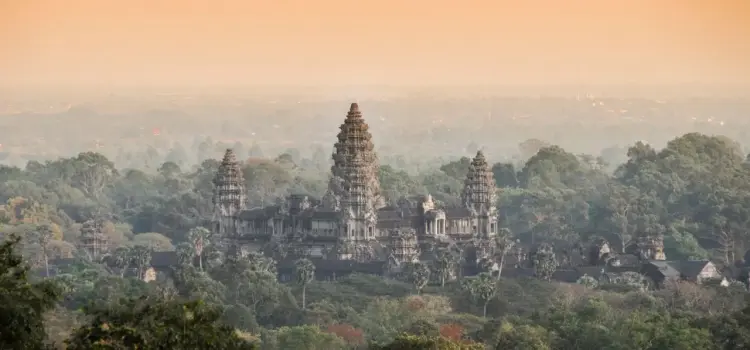 Angkor Wat temple complex rising majestically above lush jungle canopy at golden hour in Siem Reap