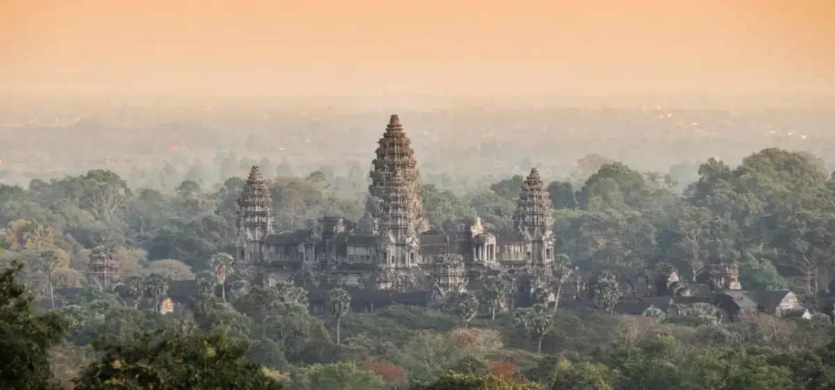 Angkor Wat temple complex rising majestically above lush jungle canopy during golden hour in Siem Reap