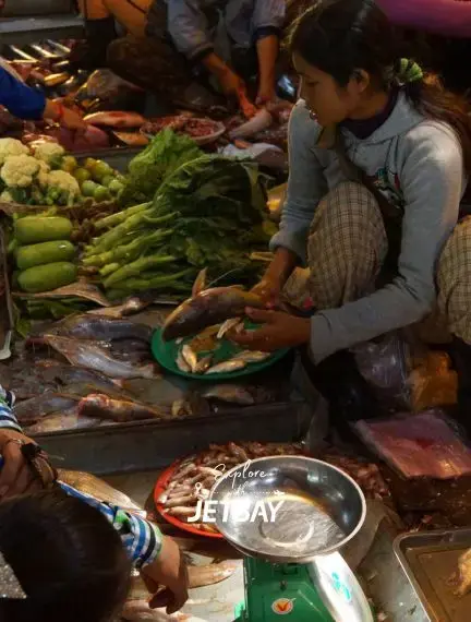 Local vendor preparing fresh fish at bustling Siem Reap market with vegetables and traditional ingredients