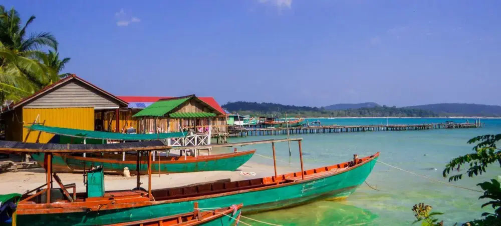 Traditional fishing boats moored in turquoise waters near colorful stilt houses in Sihanoukville, Cambodia