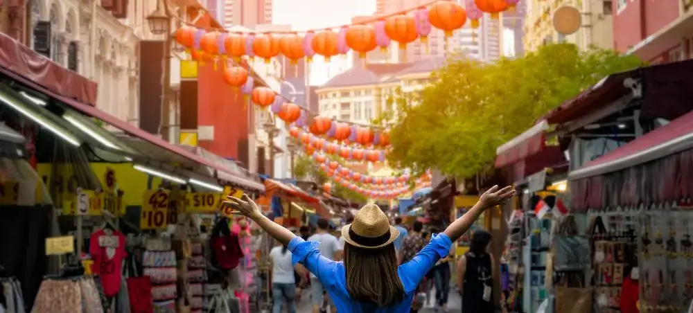 Woman with arms raised celebrating in vibrant Singapore Chinatown street market with red lanterns overhead