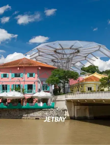 Colorful colonial buildings and modern Ferris wheel along Singapore River waterfront under blue sky