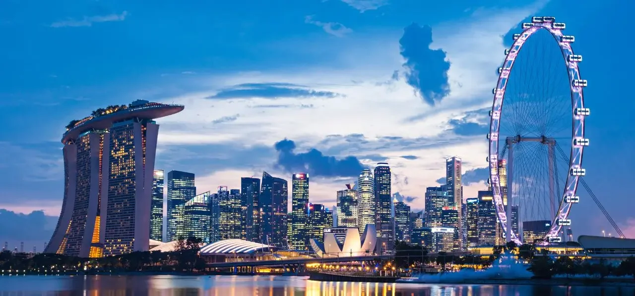 Singapore skyline at dusk featuring Marina Bay Sands, Singapore Flyer, and illuminated skyscrapers reflected in water